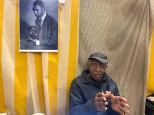 Alex Harsley, who at age 86 is still pursuing his photography passion at the East 4th St Gallery, sits before a photo of himself as a young man. Photo: Christian Spencer