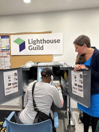 Ariel Merkel, the ADA coordinator for the NYC Board of Elections, supervises a visually impaired person practicing on a ballot marking device at the Lighthouse Guild. Every polling place in the state is able to offer the technology. Photo: Vanessa Torres