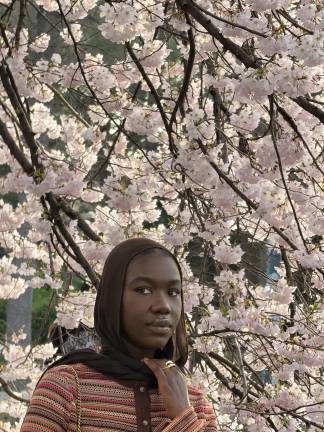 A young woman poses for a photo with cherry blossoms as the backdrop.