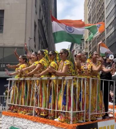 Sunglasses-wearing women in yellow, and many other colors under the sun, ride a float.