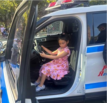 Stella gives a serious expression as she sits in the driver’s seat of police cruiser.