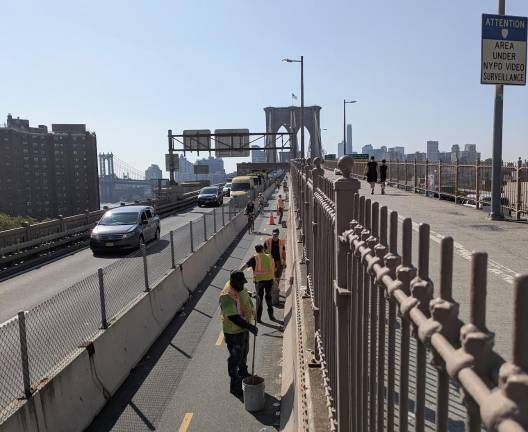 Brooklyn Bridge on July morning 2025: DOT workers on bike lane left, pedestrian path right.