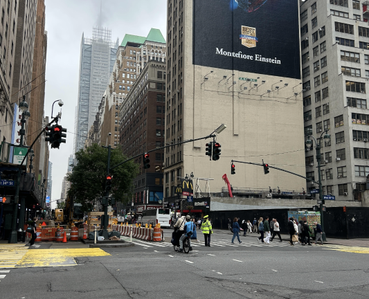Two e-bikers run a red light as a Traffic Officer faces the other way on intersection of W. 34th and 8th Ave. The quality of life pilot program included the seizure of 185 e-bikes, mopeds, and scooters in the first 60 days, the NYPD said.
