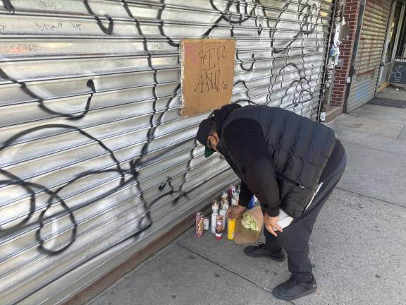 Jack Lugo, a neighborhood resident who put up the handwritten sign, lights a candle in memory of deli worker Abdu Saleh who was killed on April 25.