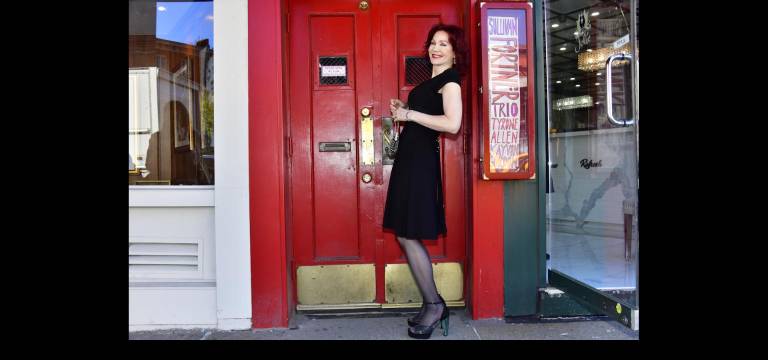 Karen Rempel leans against the Village Vanguard’s customary, beloved hand-lettered sign showing the names of the current week’s jazz performers.
