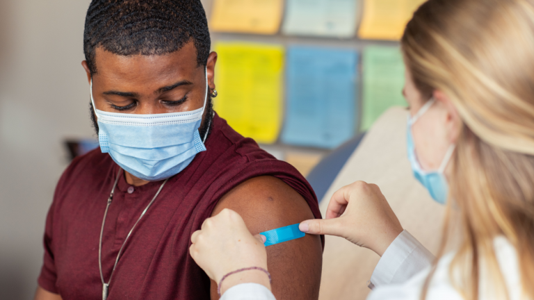 A healthcare provider places a bandage over a patient’s flu vaccine injection site.